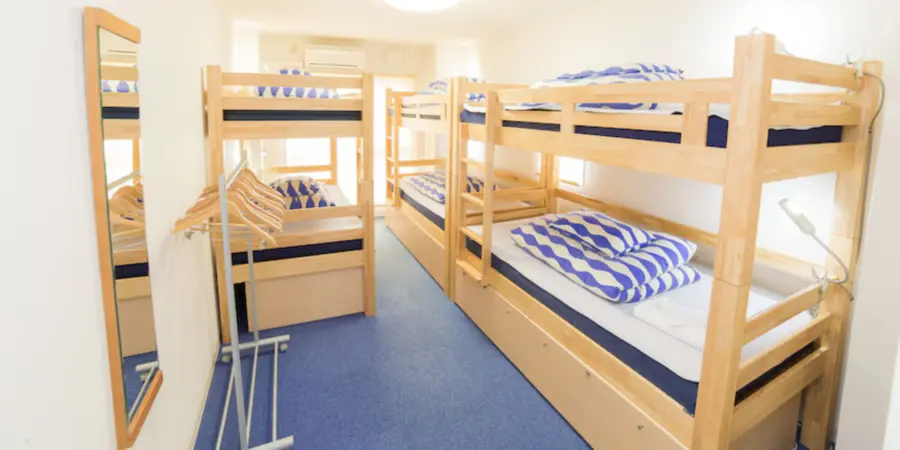 The interior of one of the dormitory rooms of Backpackers Hostel. There are wooden bunkbeds and white mattresses with blue checkered blankets.