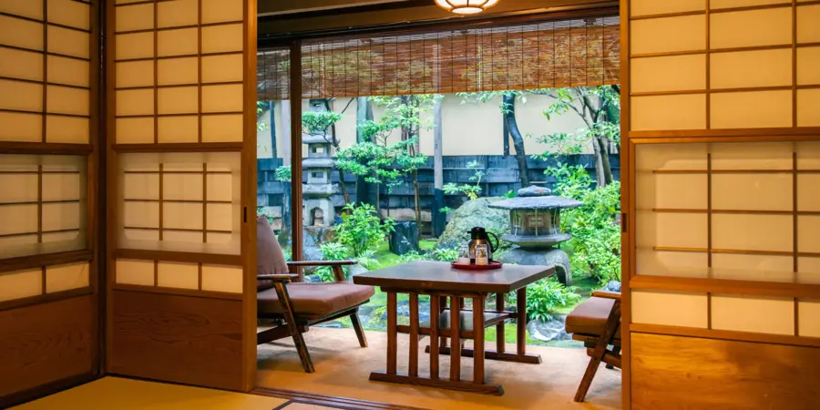One of the rooms of Hiiragiya Ryokan with a balcony-like area with lounge chairs. A lush garden is the view.
