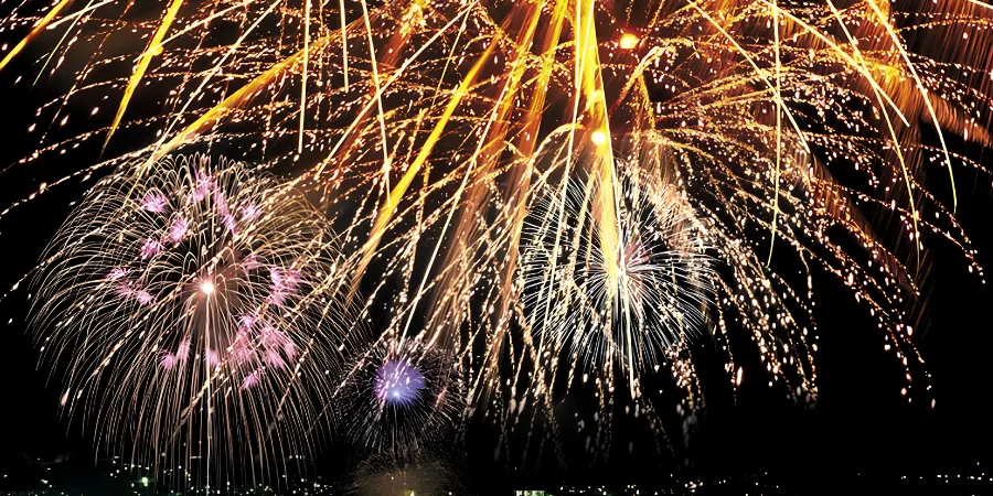 Fireworks explode over the waterfront during the Sasebo Seaside Festival, illuminating the night sky with golden, white and pink bursts.