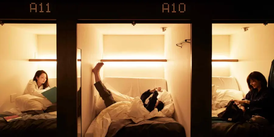 The capsule pods of The Millenials Kyoto hostel. Each pod has a guest relaxing in it, surrounded by dim lighting and comfy blankets.