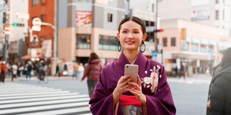 Smiling woman in a purple kimono holding a smartphone at a Tokyo street crossing