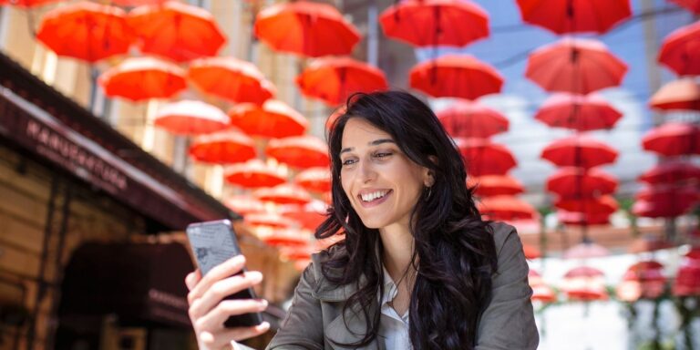 Smiling woman holding her phone beneath a canopy of red umbrellas