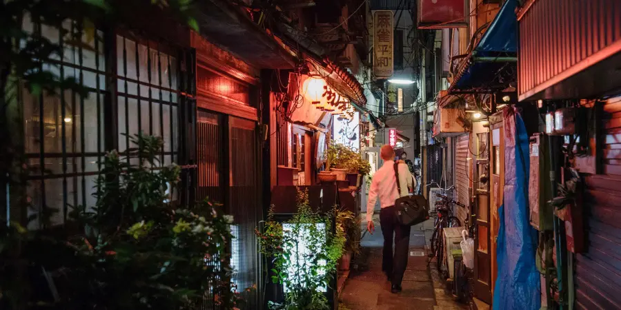 A Japanese businessman walks through a dim alley at night.