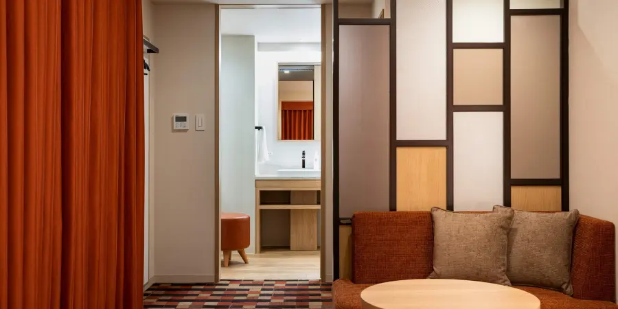 The interior of one of the suites in JR-EAST HOTEL METS KOENJI. It's minimalistic, neat, and consists of orange interior design.