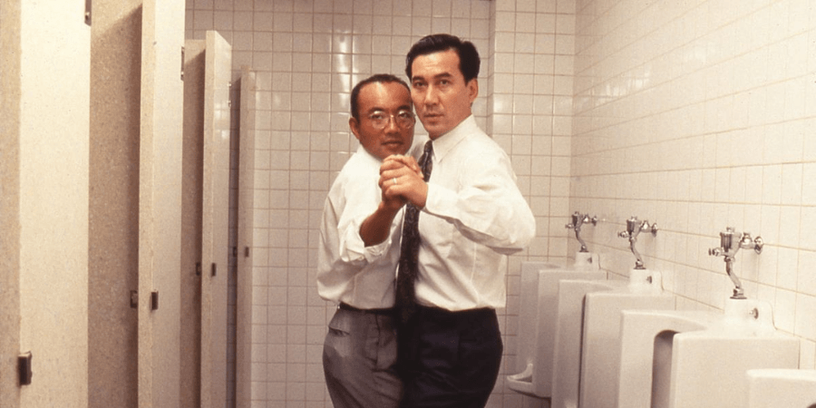 Two Japanese salarymen, Shohei Sugiyama and Tomio Aoki, practicing a formal dance posture and footwork in the fluorescent-lit men's bathroom at their office.