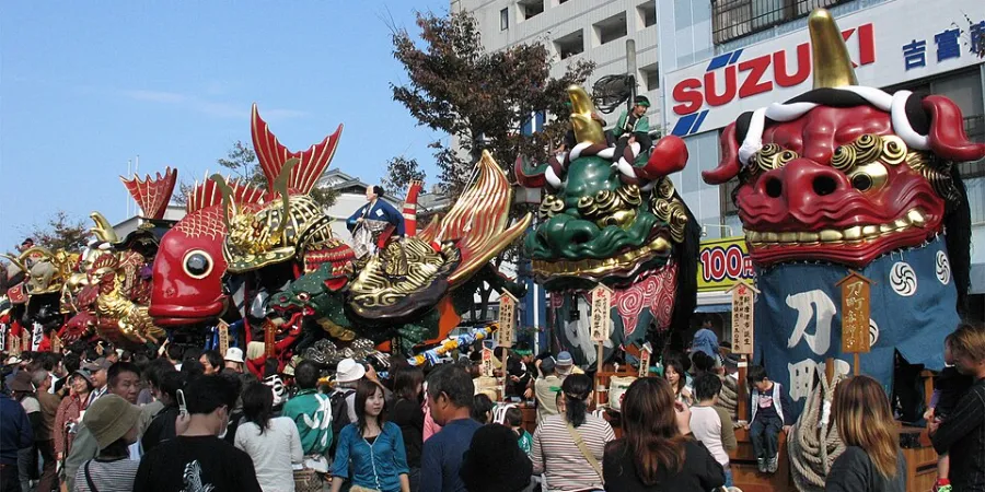 Large colorful traditional festival floats carried through a crowded street at the Karatsu Kunchi Festival in Japan