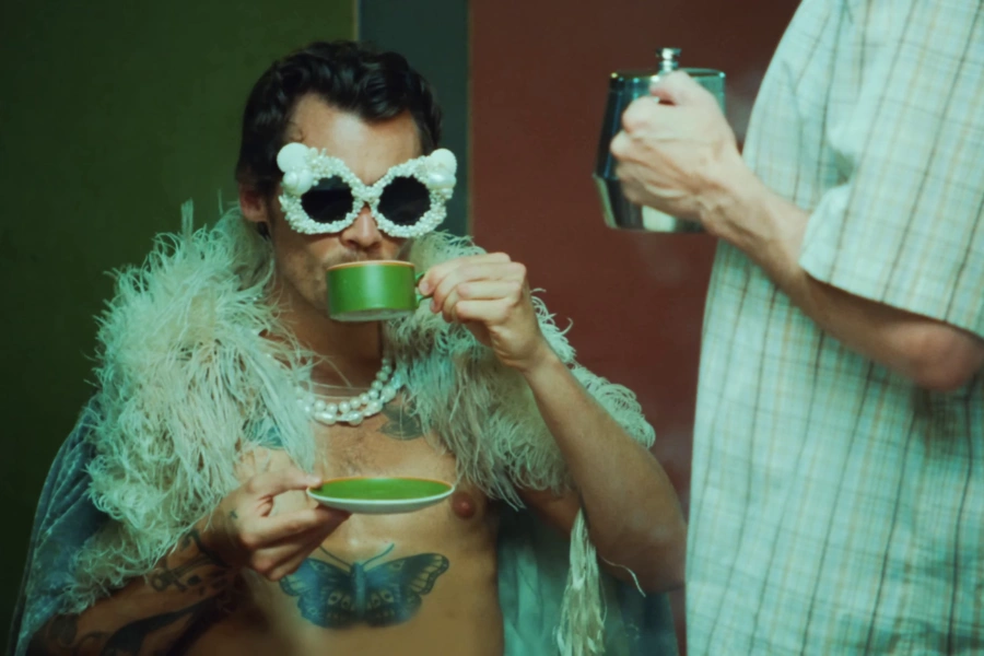 A person in eccentric fashion and pearl sunglasses drinking from a green tea cup illustrating the naturally vivid green hue of matcha. This visual aesthetic is a centerpiece of TikTok and Instagram trends where iced matcha lattes symbolize a soft clean and productive lifestyle.