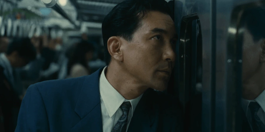 A close-up shot of Shohei Sugiyama's face (Kōji Yakusho) as he stares blankly outside the window of a metro train, reflecting his deep melancholy and discontent.