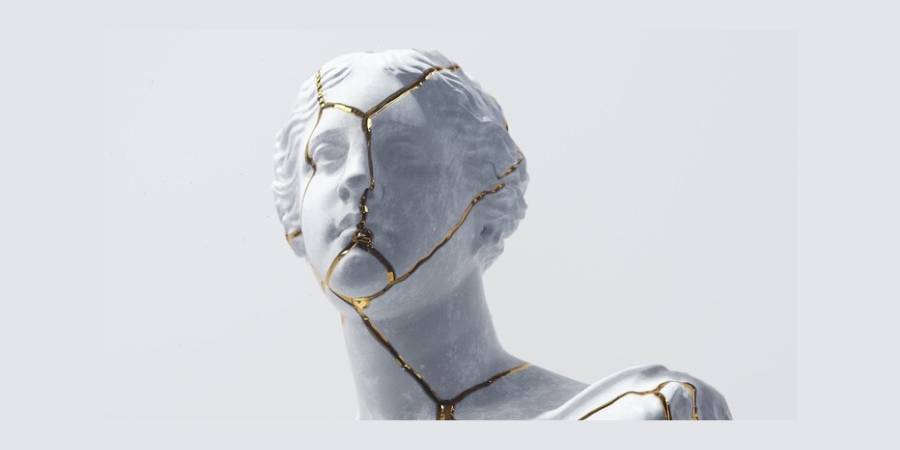 Close-up of a broken white classical sculpture (bust) that has been repaired using the Japanese art of Kintsugi, where the cracks are emphasized with bright gold lacquer.