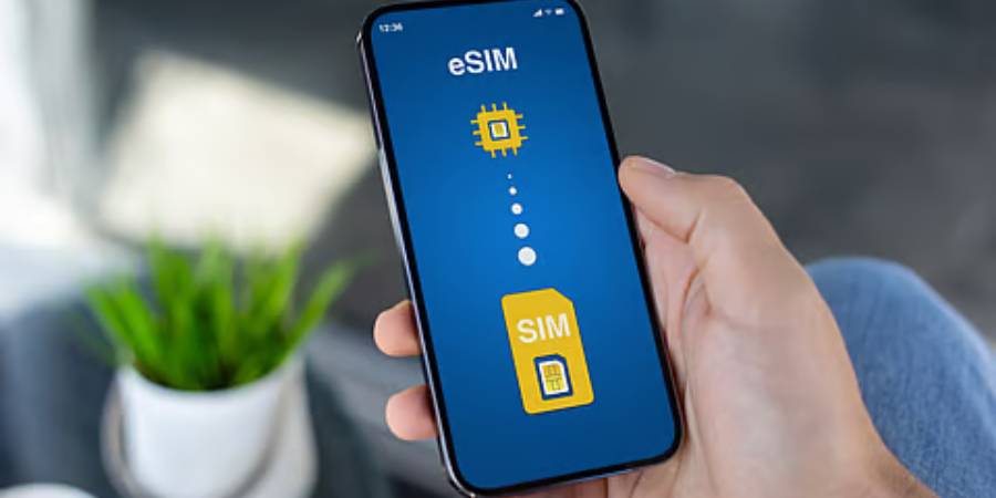 A close-up of a person holding a smartphone with a dark blue screen. The display features a vertical graphic showing a yellow physical SIM card at the bottom transitioning through a series of glowing white dots into a small, yellow integrated eSIM chip at the top, symbolizing the digital migration of cellular data.