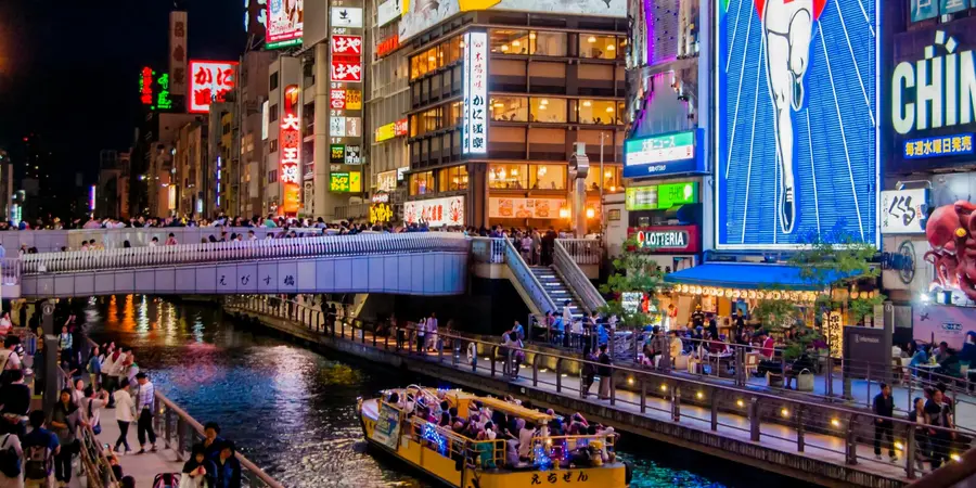 A landscape image of the Dotonbori Canal at night with the buildings clad in neon lights