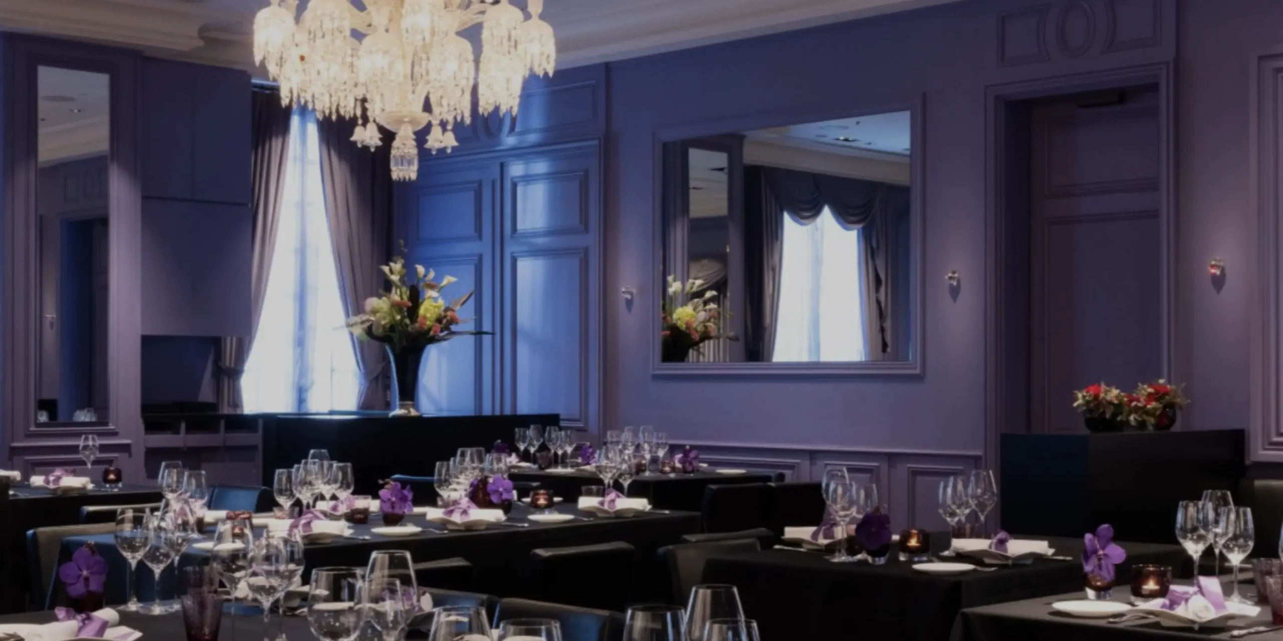 Elegant dining room at Joël Robuchon restaurant, featuring crystal chandeliers, mirrored walls, and neatly set tables with fine glassware and floral arrangements