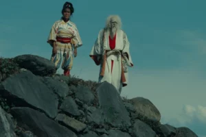 japanese cinema scene featuring two characters in traditional costume standing on rocks reflecting noh theatre influence and stylized dramatic storytelling.