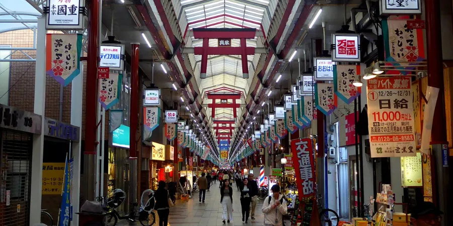 Covered Tenjinbashisuji Shopping Street arcade in Osaka, Japan, featuring traditional Japanese shop signs, pedestrians, and one of the longest shopping streets in Japan