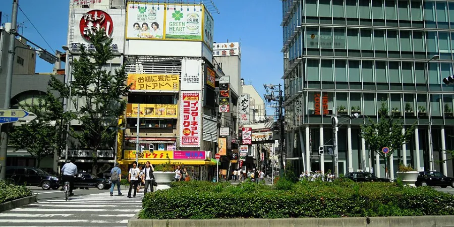Daytime street view of Umeda district in Osaka, Japan, showing modern office buildings, busy commercial streets, Japanese storefronts, and urban city life