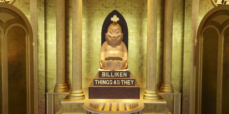 Golden Billiken statue displayed in a shrine-like alcove, with the inscription “Things As They” on its base and columns framing the illuminated backdrop