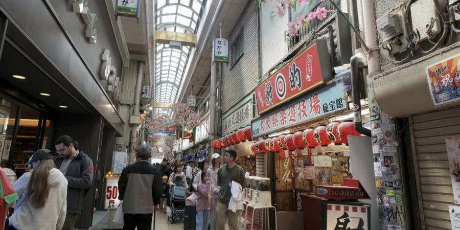 Janjan Yokocho shopping arcade in Osaka, with pedestrians passing small eateries and shops beneath a covered walkway lined with red lanterns