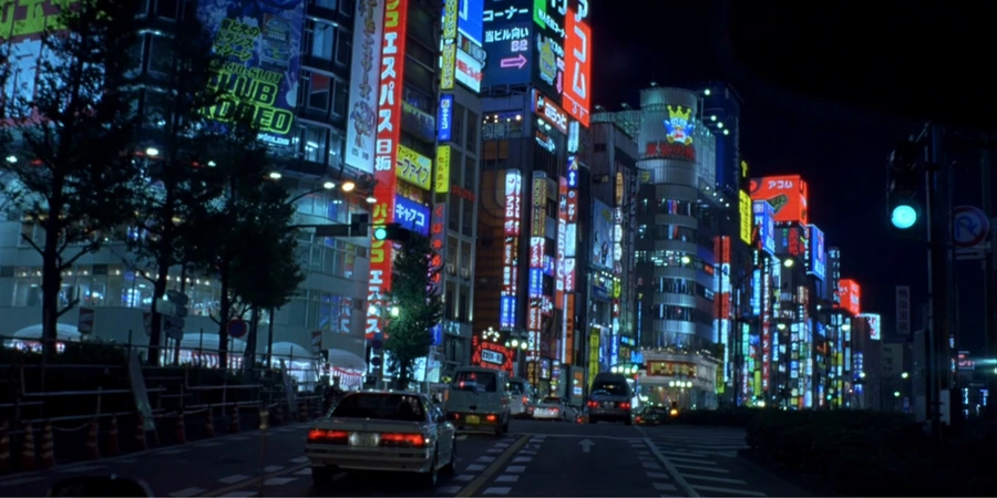 Japanese city at night, with cars driving on the streets.