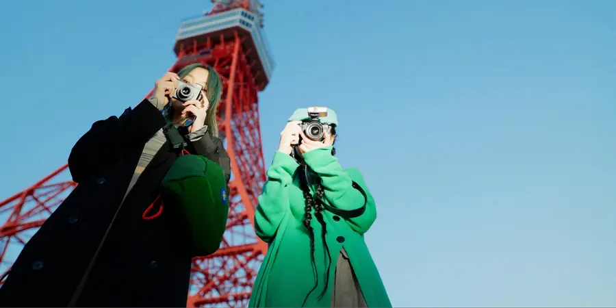 Two tourists holding cameras next to the Tokyo Tower. 