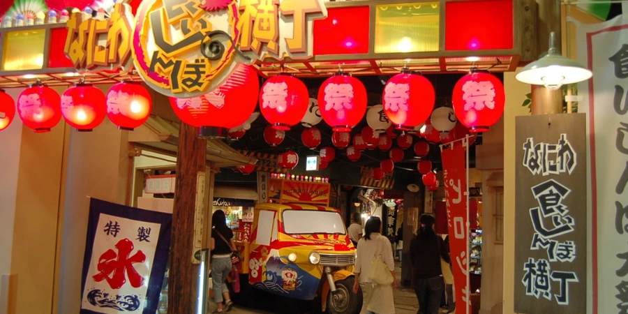 Entrance to Naniwa Kuishinbo Yokocho, lit by rows of red lanterns, with retro Osaka street displays and a small vintage-style vehicle inside