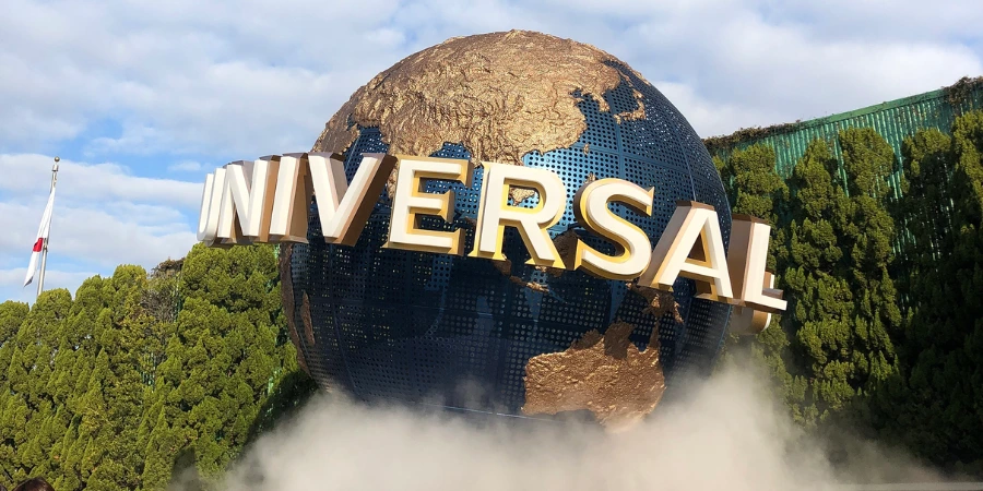 Universal Studios Japan globe fountain at the park entrance, with gold continents, mist rising at the base, and surrounding greenery