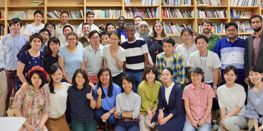 Group photo of a diverse group of international students standing and sitting together in a library, smiling at the camera with bookshelves in the background.