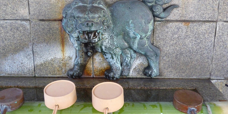 Ornate stone fountain and water basin (chozuya) at Namba Yasaka Shrine (Namba-Yasaka-Jinja) in Osaka, with flowing spring water, dragon-head spout, and resting wooden ladles for the traditional hand-mouth purification ritual before praying at the lion head shrine.