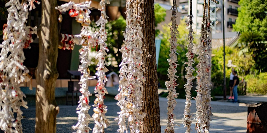 Colorful lion-shaped omikuji fortune strips tied together and hung around a tree at Namba Yasaka Shrine Osaka, quirky protective keepsakes tied to Susanoo-no-Mikoto deity, priced at 200 yen, fluttering with visitors' fortunes alongside the shrine's ema plaques and omamori charms.