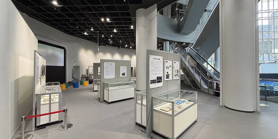 Bright, bustling interior of the 1F "Everyone's Science Lab" at Osaka Science Museum, with interactive electricity experiments, energy displays, and the prominent Gakutensoku robot replica amid visitors engaging hands-on.