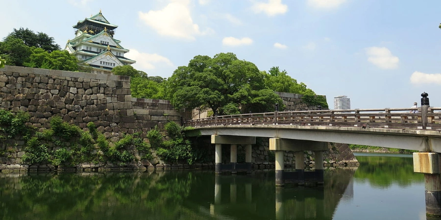 Iconic view of Osaka Castle's golden-horned main keep tower from Gokurakubashi Bridge in Castle Park, perfectly positioned near the Osaka Museum of History for combined historical visits.