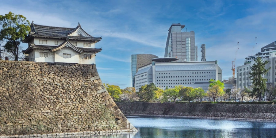 Scenic river moat separating majestic Osaka Castle from the modern Osaka Museum of History building, symbolizing the seamless blend of ancient fortress and contemporary historical exhibits.