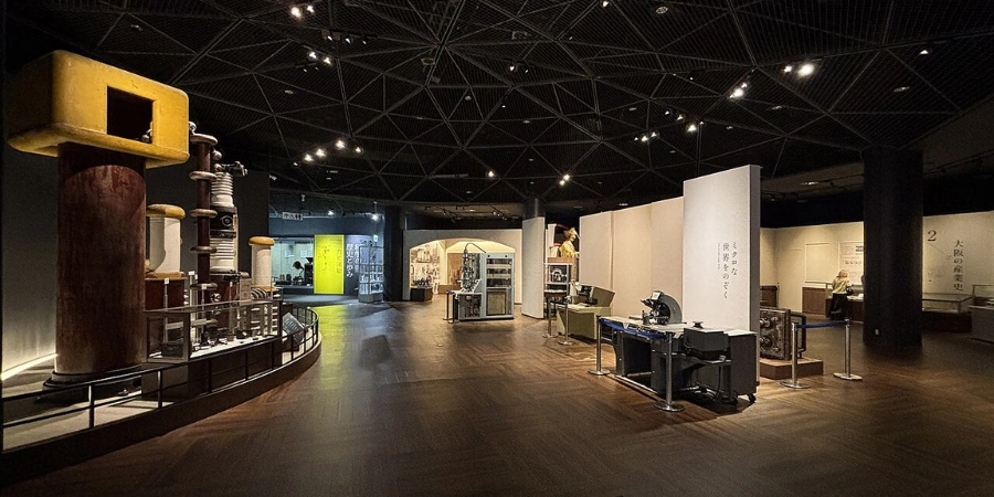 Spacious 4F "Scientific Exploration" gallery at Osaka Science Museum, filled with universe models like the Milky Way cylinder, planet weight scales, aurora simulators, and digital planispheres under high ceilings and multilingual signage.