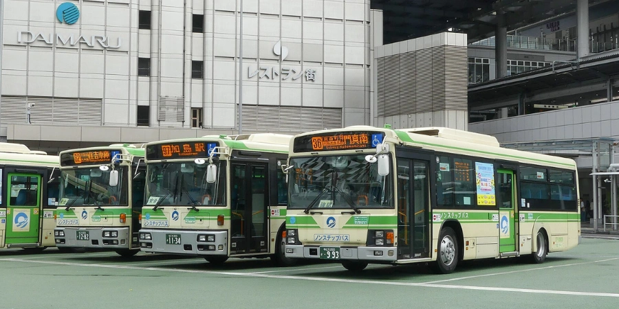 Osaka City Buses parked at Osaka Station terminal, ready for local routes, with station signage and passengers in the background.