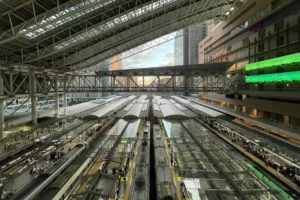 Wide-angle aerial view of Osaka Station's modern glass canopy and surrounding high-rises in Umeda, showcasing the bustling transportation and commercial hub at dusk.