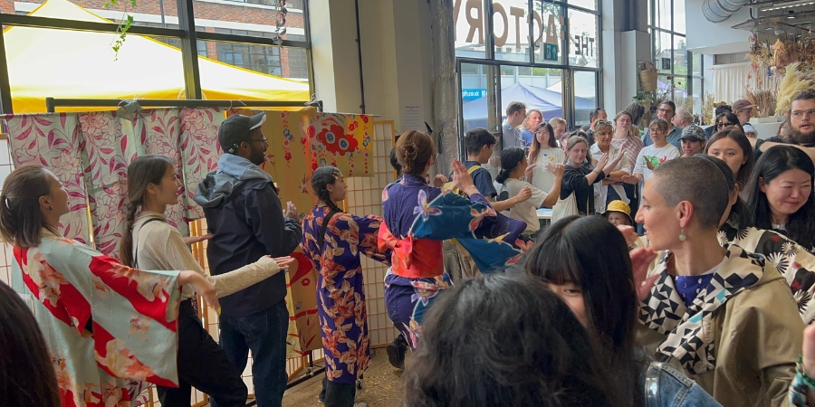 Crowd gathered indoors watching participants in colorful yukata performing a traditional Japanese festival dance at a cultural market event.