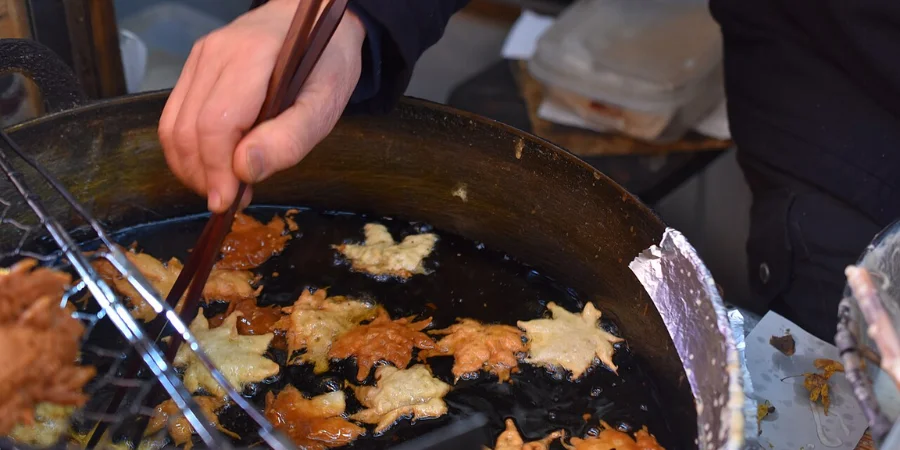 Traditional momiji tempura, deep-fried maple leaves being cooked in oil at a street food stall in Minoo, Osaka