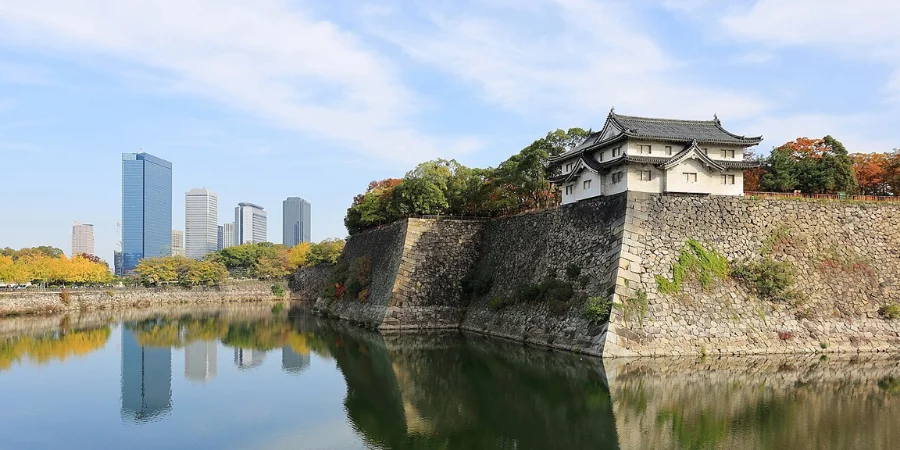 Osaka Castle with stone walls and moat reflecting the city skyline and autumn foliage in Osaka, Japan