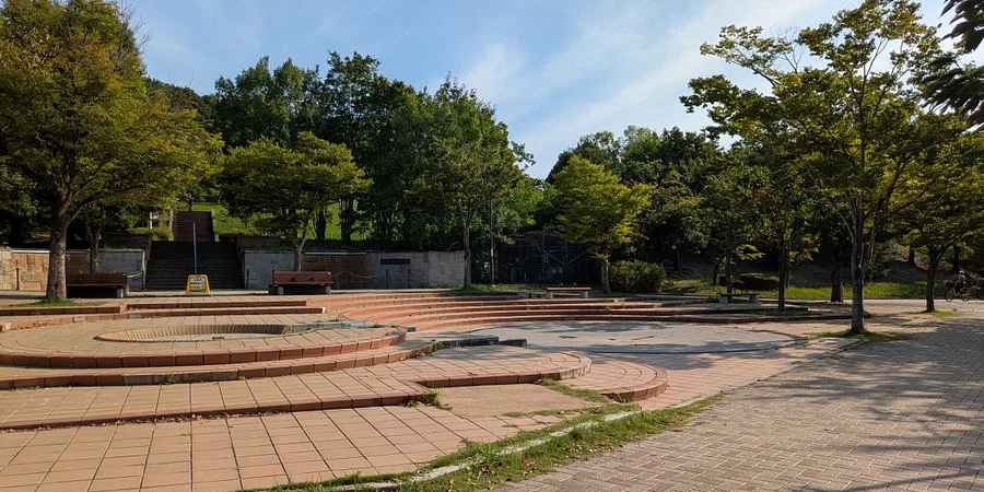 Open-air amphitheater and paved plaza at Senri Central Park in Osaka, surrounded by trees and greenery on a sunny day