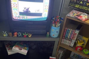 Heisei retro gaming collection featuring a vintage CRT television, Pokémon collectibles, manga, retro video games and nostalgic Japanese pop culture memorabilia.