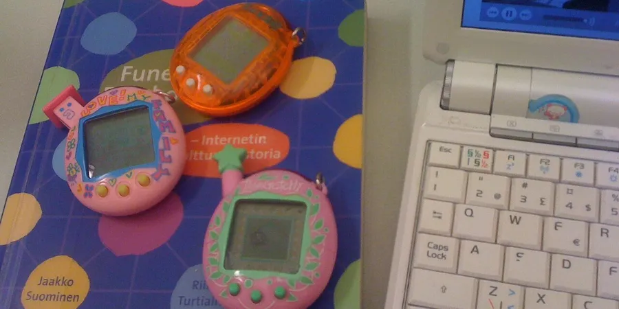 Vintage Tamagotchi virtual pet devices from the Heisei era displayed beside a retro laptop, highlighting nostalgic Japanese electronic toys.