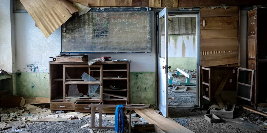 Abandoned school interior on Hashima Island, showing a damaged classroom with broken furniture, chalkboard, and debris.