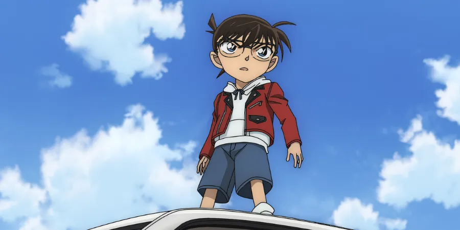 Anime still from Detective Conan M29 showing Conan Edogawa standing on top of a car against a bright blue sky with clouds.