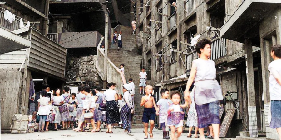 Historical photo of Hashima Island residents and children gathered between concrete apartment blocks during the island’s mining era.