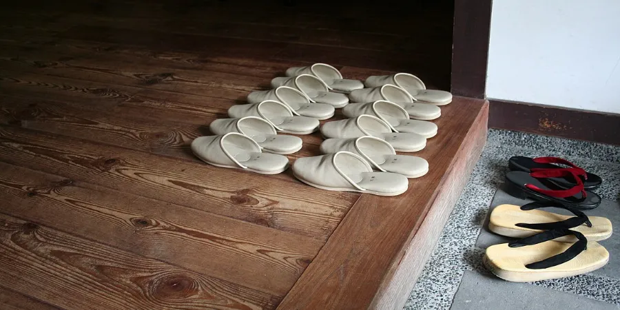 House slippers neatly lined up on a wooden entryway floor beside outdoor sandals, illustrating Japanese home etiquette and shoe removal customs.