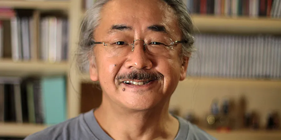 Nobuo Uematsu's portrait in front of shelves, suitable for content about Final Fantasy music, Square Enix soundtracks, and game composition.