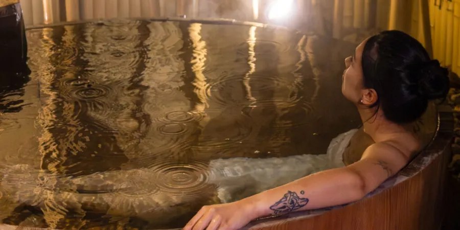 Woman with visible tattoos relaxing in a Japanese onsen bath, illustrating tattoo etiquette and hot spring customs in Japan.