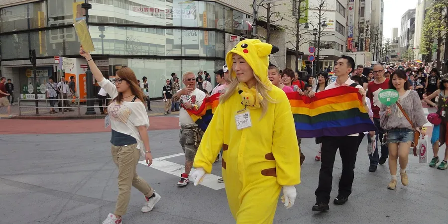 Tokyo Pride Parade participants walking through the city with a rainbow flag and colourful costumes.