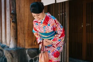 Woman in a colourful kimono bowing politely outside a traditional Japanese building, demonstrating Japanese etiquette and respectful greetings.