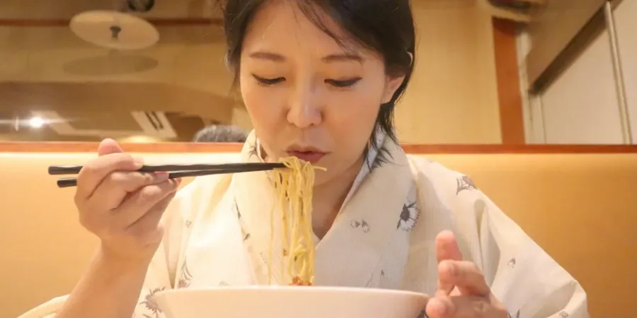 Woman eating ramen with chopsticks in a Japanese restaurant, showing casual dining etiquette and noodle culture in Japan.