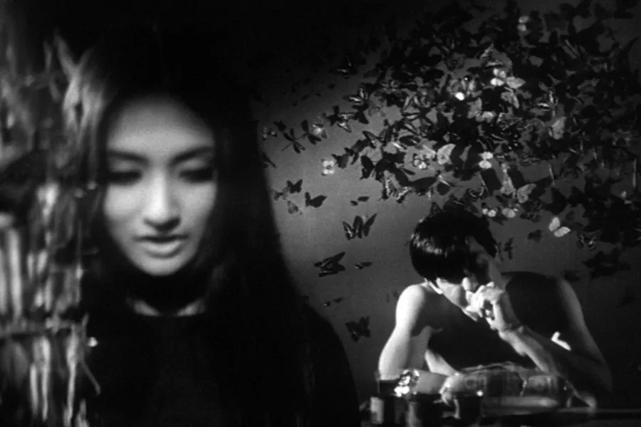 Dreamlike scene from Branded to Kill (1967) featuring a woman in the foreground and a hitman beneath butterfly-covered walls in Seijun Suzuki's surreal Japanese New Wave crime film.